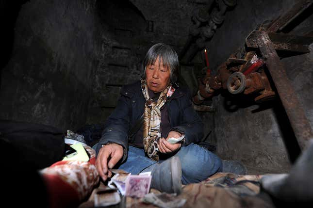 Quan Youzhi, 66, counts money in her dwelling inside an underground shaft in Beijing, December 5, 2013. According to local media, around five underground shafts, in which people were living in, were blocked by city officials on Friday morning at a neighbourhood in Beijing. One of the dwellers, Quan Youzhi, 66, has been living in the shafts, which were originally used for the city's heating system, for around 20 years as she could not afford to pay rent for housing after she came to Beijing, and has since relocated several times after being chased away by law enforcement officials. Quan supports herself with about 10 yuan ($1.64) daily, which she makes from collecting waste bottles. Picture taken December 5, 2013.