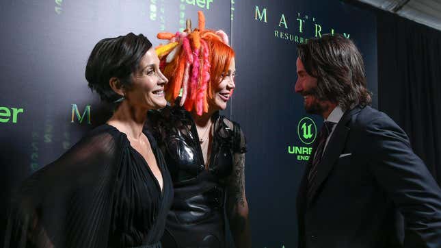 Carrie-Anne Moss in a plunging black dress, Lana Wachowku with orange/pink-yellow hair, and Keanue Reeves in a normal suit.