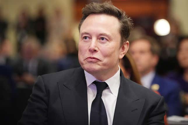 Elon Musk wearing a suit and tie smiling and looking upwards