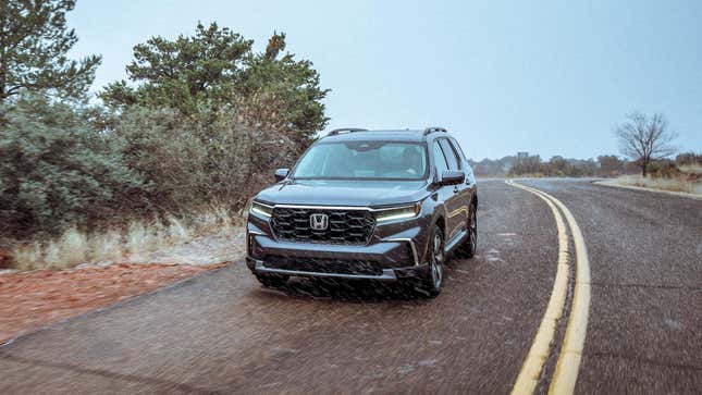 A gray Honda Pilot driving on a two-lane road in light snow