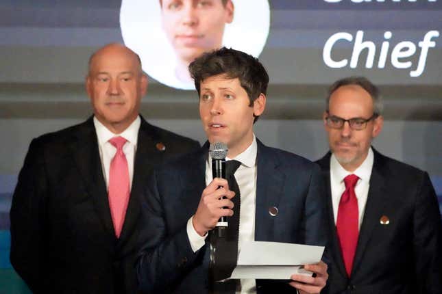 business new tamfitronics sam altman wearing a white button down and black tie and suit speaking into a microphone with two men behind him in front of a backdrop