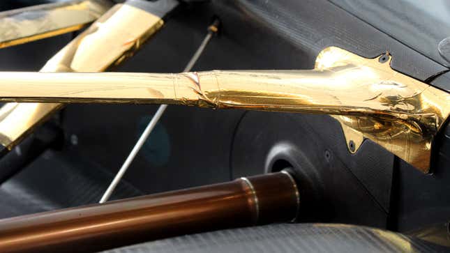 A photo of the rear suspension of a 1990s McLaren F1 car, which is wrapped in gold. 