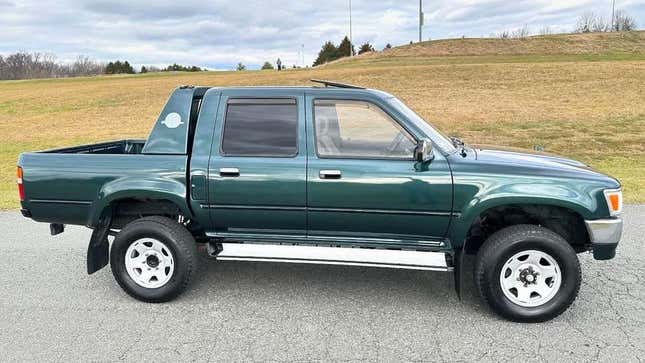 a side view of the dark green Hilux in front of grassy hills