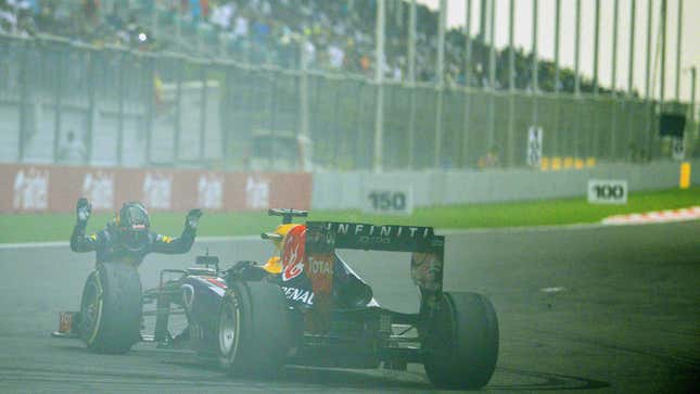 A photo of Sebastian Vettel bowing in front of his Red Bull Formula 1 car. 