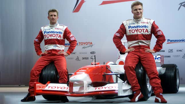 A photo of two race drivers sat on the wheels of a red and white Toyota F1 car. 