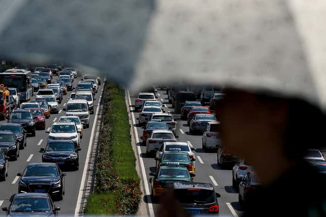 FILE - A woman walks past vehicles on a city ring-road clogged with heavy traffic in Beijing on Aug. 13, 2019. China&#39;s auto exports surged 63.7% in 2023 while sales at home, boosted by year-end incentives, rose 4.2%, an industry association said Thursday, Jan. 11. (AP Photo/Andy Wong, File)