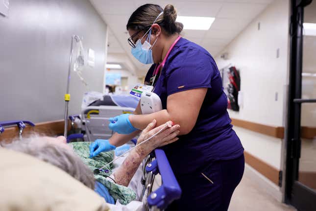 A registered nurse cares for a patient on a stretcher in a hallway of a California hospital