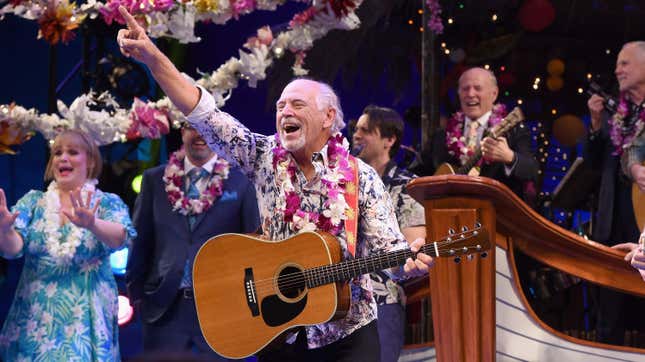 Jimmy buffett holding a guitar and pointing into the air after a show