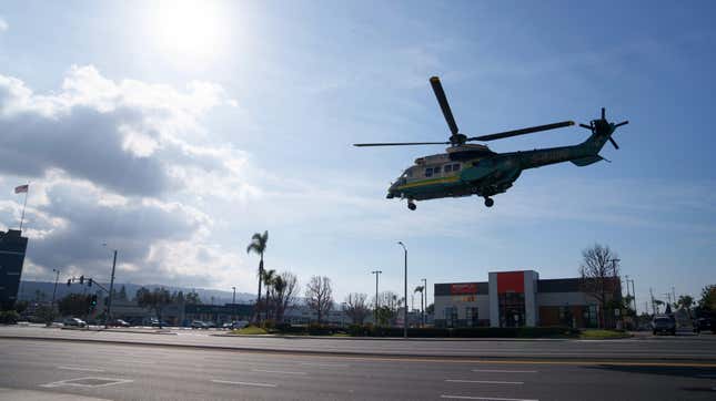 Law enforcement take off in a helicopter near a white van in a parking lot 