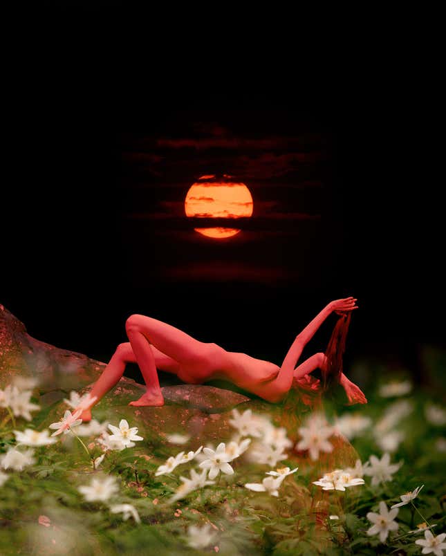 A naked woman lies on her back with a red sun in the background.