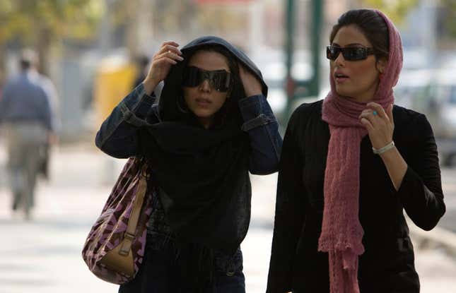 Women adjust their headscarves as they walk along a sidewalk in Tehran.