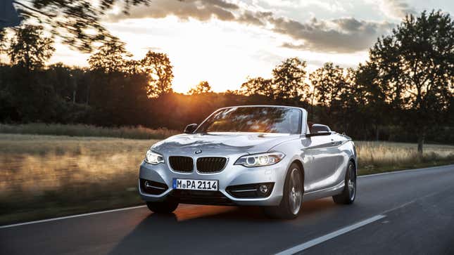 A photo of a BMW 228i convertible driving on a road. 