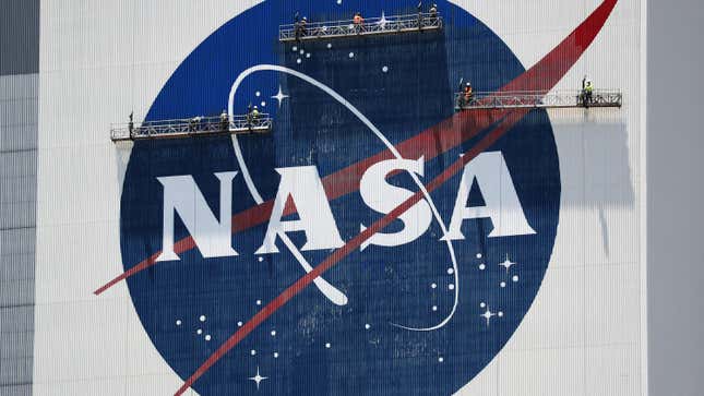 workers hanging on cranes in front of the NASA logo