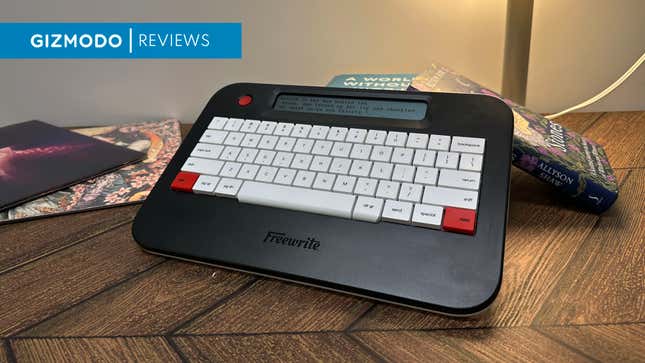 A FreeWrite Alpha in black with three red keys surrounded by books and album covers.