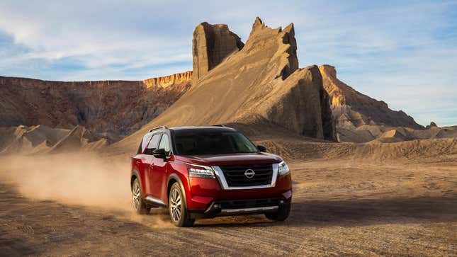 A red nissan pathfinder driving on dirt in front of a big rock formation