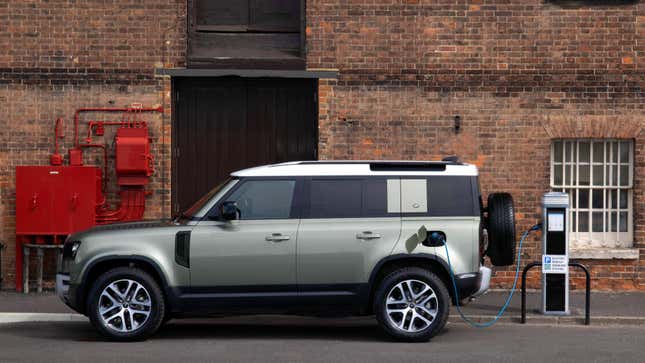 A side view of a land rover defender PHEV charging in front of a brick building