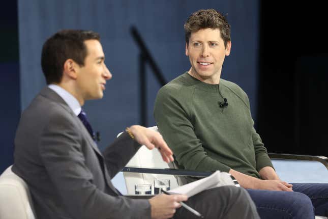 Andrew Ross Sorkin's side profile as he's speaking and holding his hand up while Sam Altman wears a green shirt and jeans and smiles at him from his seat