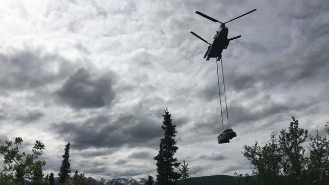 A photo of a chinook flying with a bus hanging below it. 
