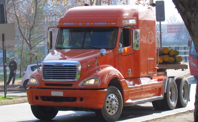An orange Freightliner Columbia truck towing a load of logs