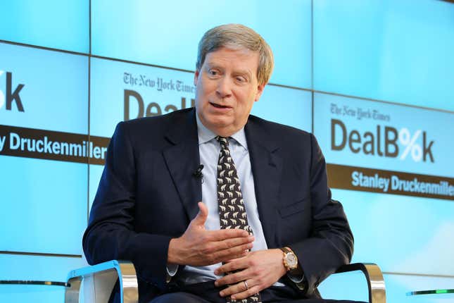 stanely druckenmiller wearing a suit jacket and tie with a blue button down sitting with a DealBook backdrop behind him