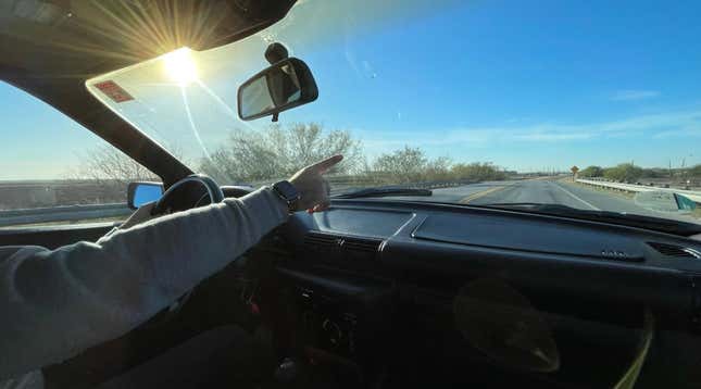 Someone is pointing through the windshield of a car off into the distance.