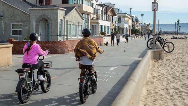 A photo of people riding electric bikes near the beach. 