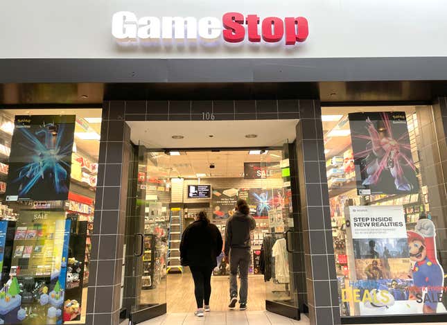 A GameStop storefront in a mall with two people walking in