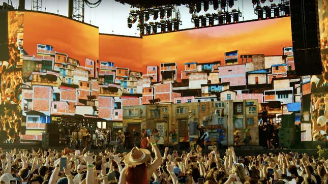 A Coachella crowd waves their arms in the air in front of a colorful stage set for artist Anitta.