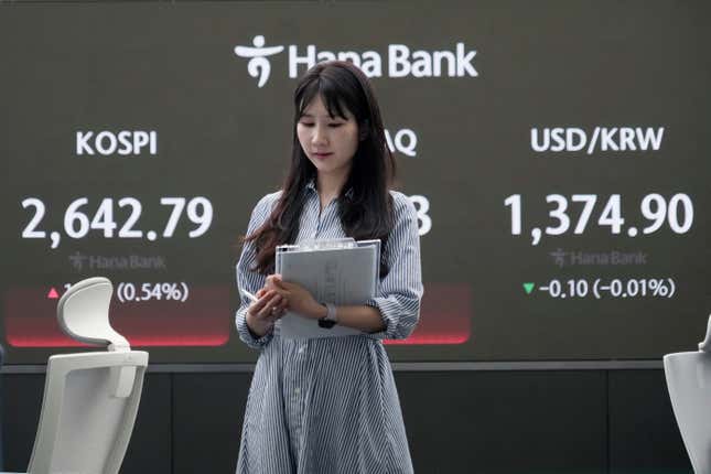 A currency trader passes by the screen showing the Korea Composite Stock Price Index (KOSPI), left, at the foreign exchange dealing room of the KEB Hana Bank headquarters in Seoul, South Korea, Friday, April 26, 2024. Asian shares mostly rose Friday despite worries about the economic outlook and inflation in the U.S. and the rest of the world. (AP Photo/Ahn Young-joon)