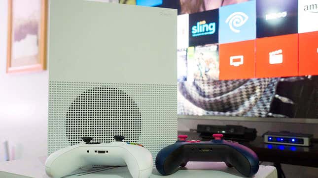 The Xbox One S and its controllers in front of a TV. 