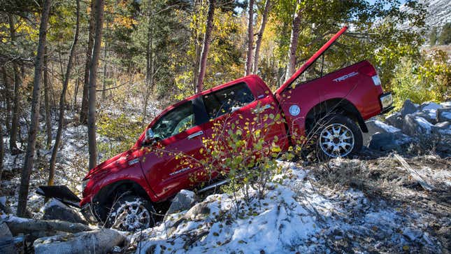 A photo of a red pickup truck crashed into a forrest. 