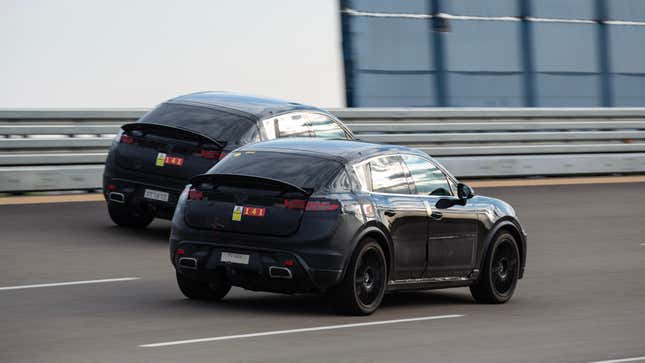 Rear 3/4 view of two camouflaged Porsche Macan EVs driving on track