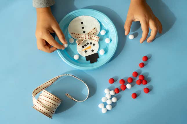 Hands of child making a snowman with ribbon and pom pom at Christmas time in a domestic room, Italy