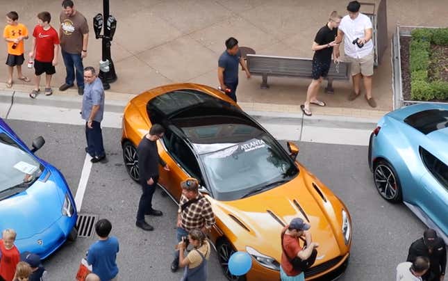 Man touches an orange Aston Martin at a crowded car show