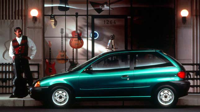 A photo of a guitar player looking longingly at a Geo Metro hatchback. 