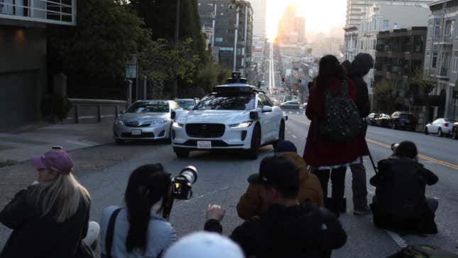 A Waymo self-driving car stops while driving as people stand in the middle of the street to photograph the sunrise on April 09, 2024 in San Francisco, California.