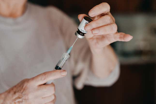 Close up of senior woman’s hands close up while filling a syringe with medicine.