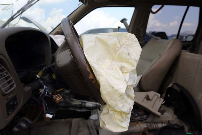 A light yellow air bag emerges deflated from a steering wheel inside a wrecked car.