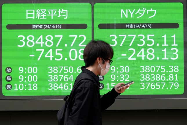 A person walks in front of an electronic stock board showing Japan&#39;s Nikkei and New York Dow indexes at a securities firm Tuesday, April 16, 2024, in Tokyo. (AP Photo/Eugene Hoshiko)