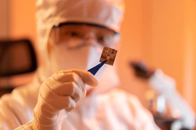 person in hazmat suit and goggles holding up a wafer chip