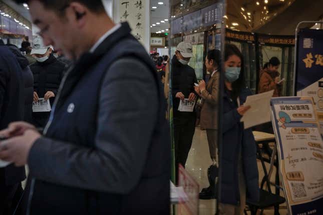 Chinese job seekers hold brochures is reflected on a mirror as they look for job vacancies at a job fair in Beijing on Feb. 23, 2024. China&#39;s efforts to restore confidence and rev up the economy will top the agenda during this month’s meeting of the ceremonial national legislature. (AP Photo/Andy Wong)