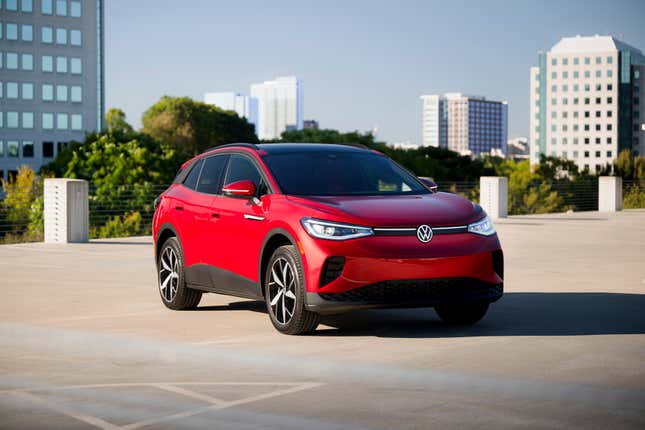 A red VW ID.4 electric suv sits on a parking deck with tall buildings in the background.