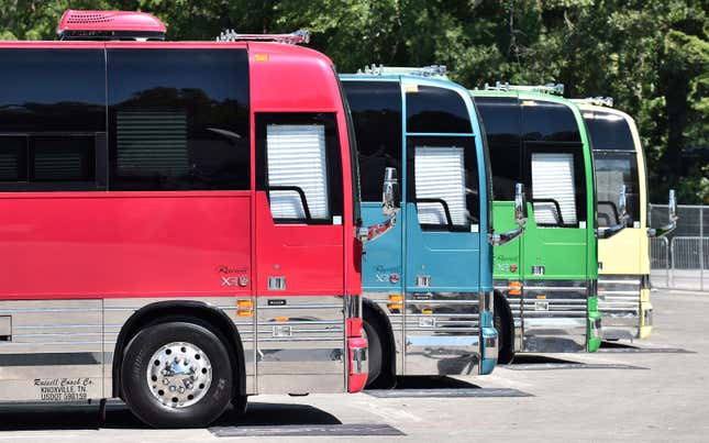 A photo of four brightly colored tour buses at a music festival. 
