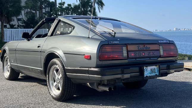 Una toma trasera de 3/4 de un Datsun 280ZX Turbo gris estacionado frente al agua