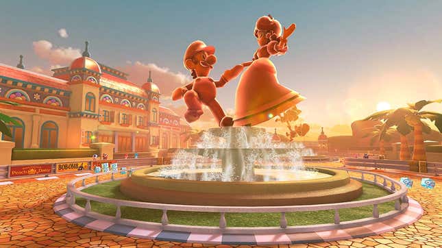 A screenshot of a track from Mario Kart 8 Deluxe's final wave of DLC. A statue of Luigi and Daisy sits at the center of a fountain as the sun sets behind them.