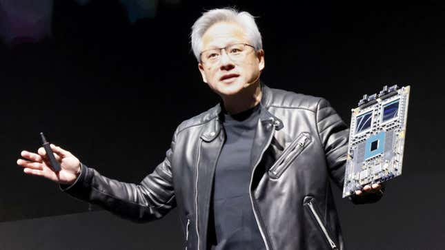 Jensen Huang speaking while wearing a black t shirt and leather jacket holding up a chip