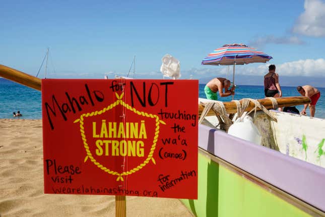 FILE -A man sets up an umbrella in front of a Lahaina Strong informational sign, Wednesday, Dec. 6, 2023, Kaanapali Beach in Lahaina, Hawaii. An acute housing shortage hitting fire survivors on the Hawaiian island of Maui is squeezing out residents even as they try to overcome the loss of loved ones, their homes and their community. (AP Photo/Lindsey Wasson, File)