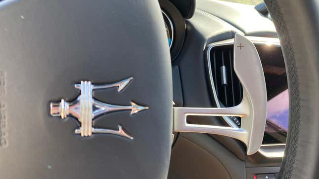 A close-up of the upshift paddle with the Maserati trident on the steering wheel pointing at it