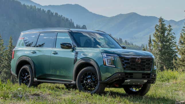 A photo of a teal Armada Pro-4X parked on grass in front of trees and mountains