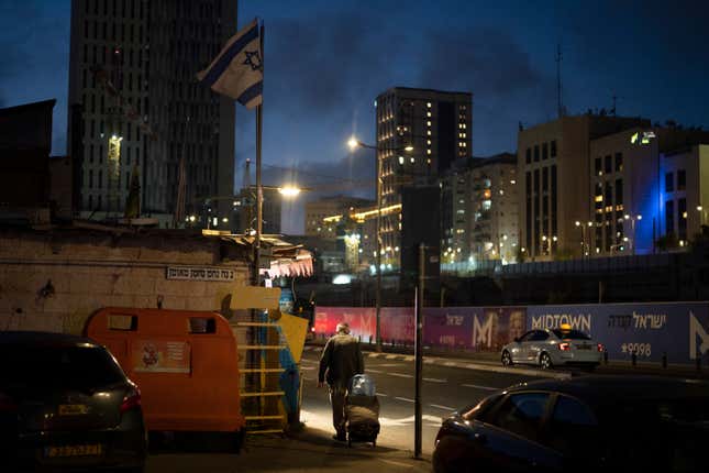 An elderly Jewish man pulls his cart on a street during the dusk in Jerusalem, Sunday, April 14, 2024. Israel on Sunday hailed its air defenses in the face of an unprecedented attack by Iran, saying the systems thwarted 99% of the more than 300 drones and missiles launched toward its territory. (AP Photo/Leo Correa)